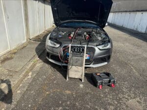 Audi grise RS, capot ouvert, reliée à une machine Dumas Décalaminage. Plaque 31 visible. Outils sur asphalte devant garages.